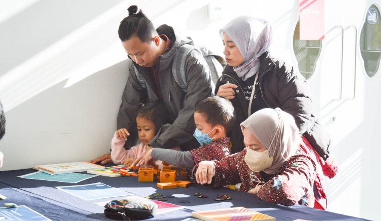 A group of  3 adults and 2 children interact with maths puzzles on a table