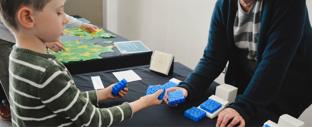 A child holds two blue 3D printed lattices across the table from an adult.