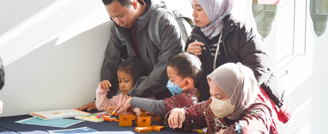A group of 3 adults and 2 children interact with maths puzzles on a table