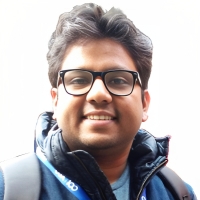 Sourav Patranabish smiling at the camera, wearing glasses and a blue coat